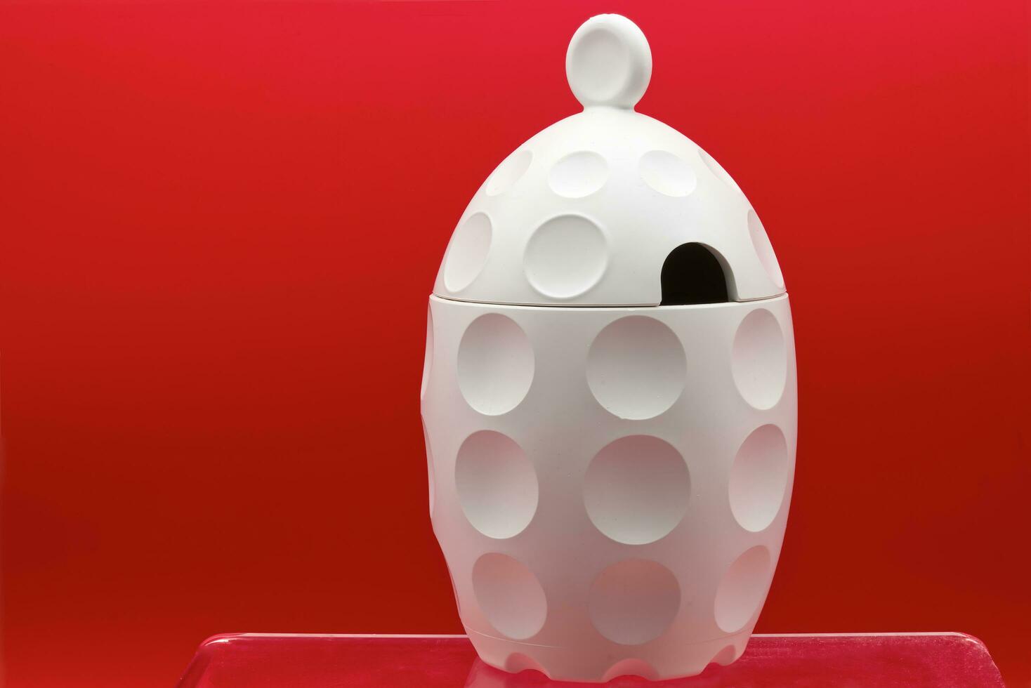 Bologna  Italy  May 23, 2023 A white sugar bowl isolated on red background. Design object for kitchen made in Italy by Guizzini with recycled material. photo