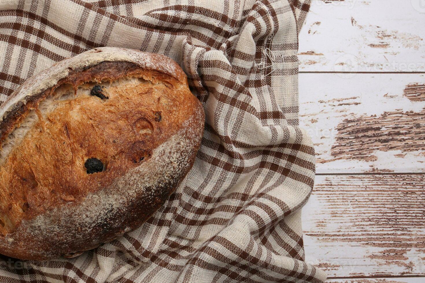 Rustic whole grain artisan bread loaf with cranberry raisin dry fruit nuts wrapped in checkers cloth with wooden table top flat lay view photo