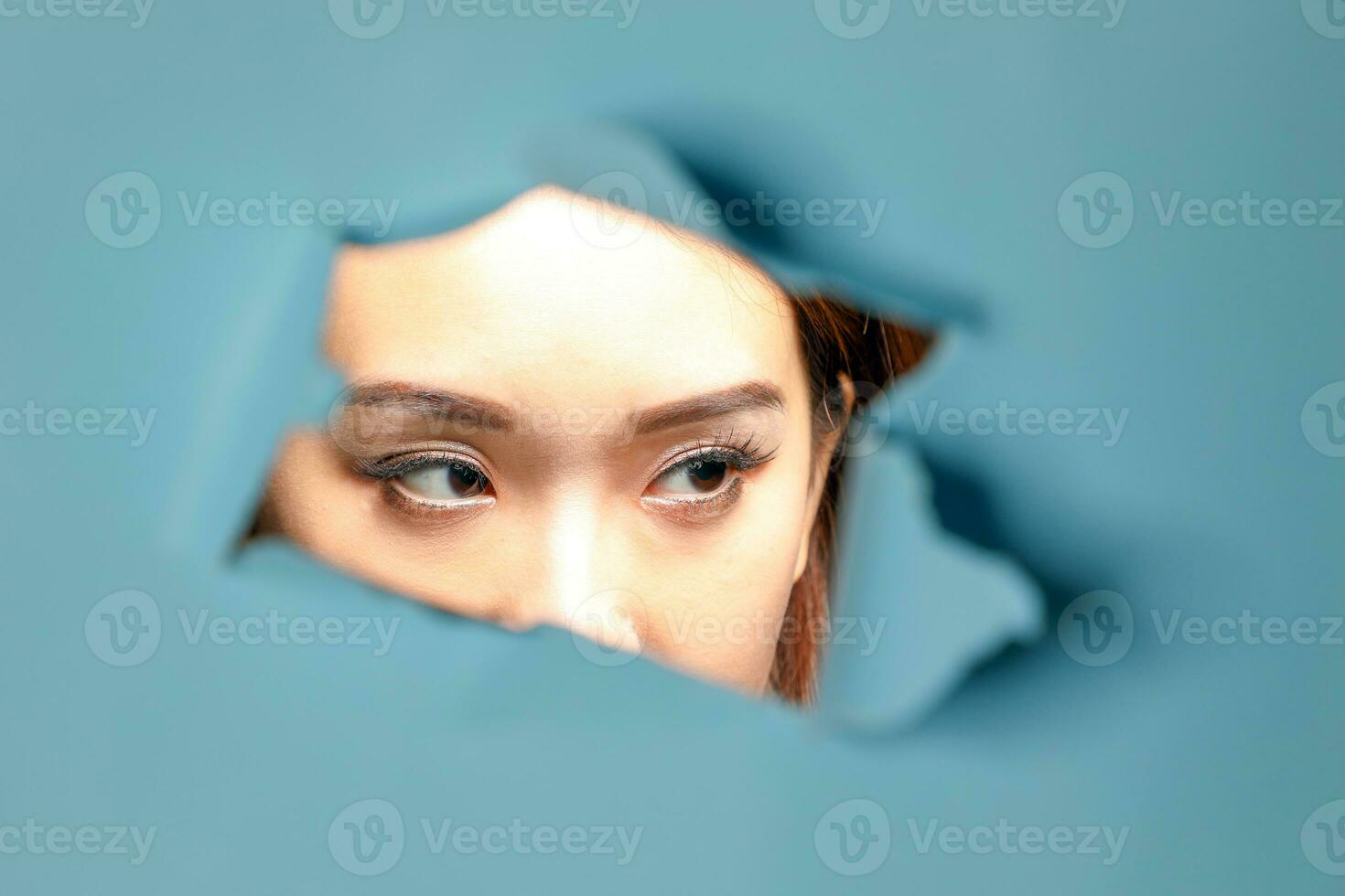 Young beautiful Asian woman expression through torn paper hole photo