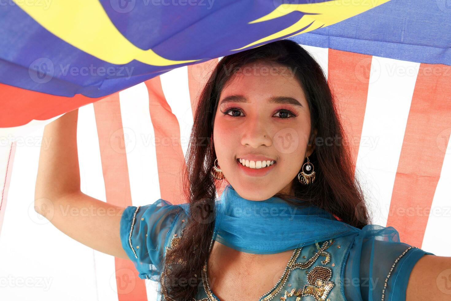 South east Asian Indian race ethnic origin woman wearing Indian dress costume salwar kameez multiracial community holding under Malaysian flag Jalur Gemilang on white background photo