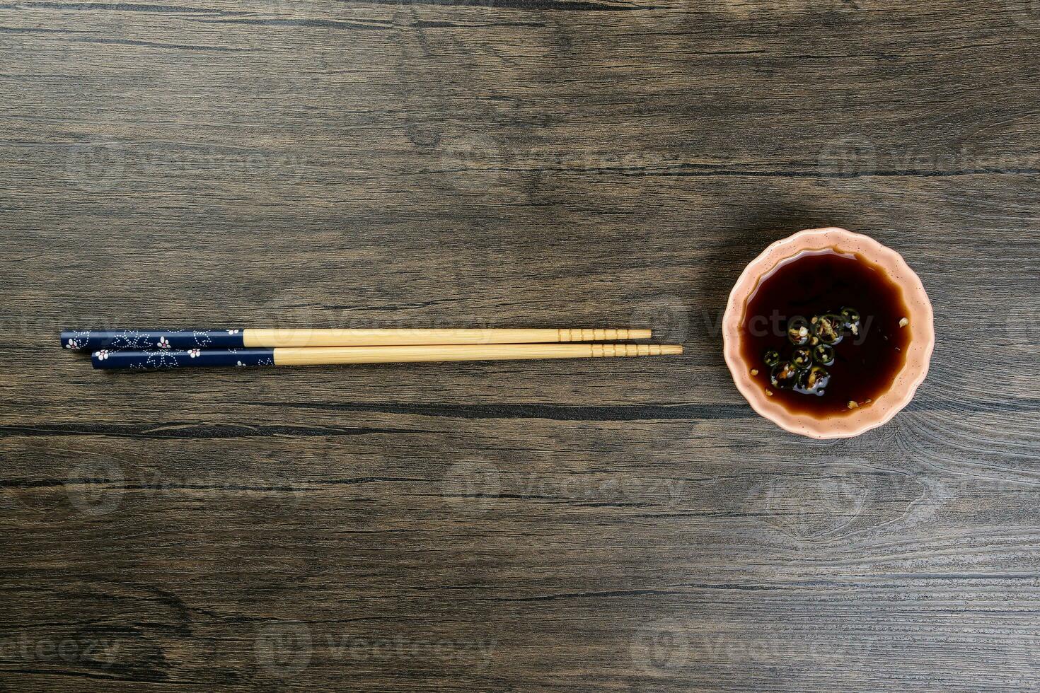 Bamboo wooden chopsticks and chili soya sauce in small ceramic bowl dish on rustic wood background photo
