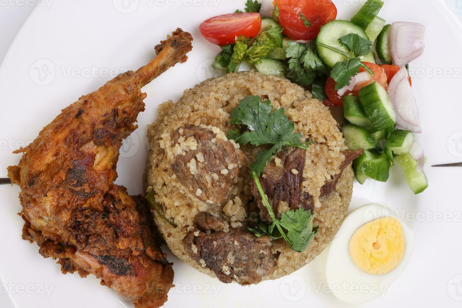 Beef Biryani Tehari with boiled egg coriander leaf garnish chicken curry pot roasted leg tomato cucumber onion chili coriander salad on white plate set over white background photo