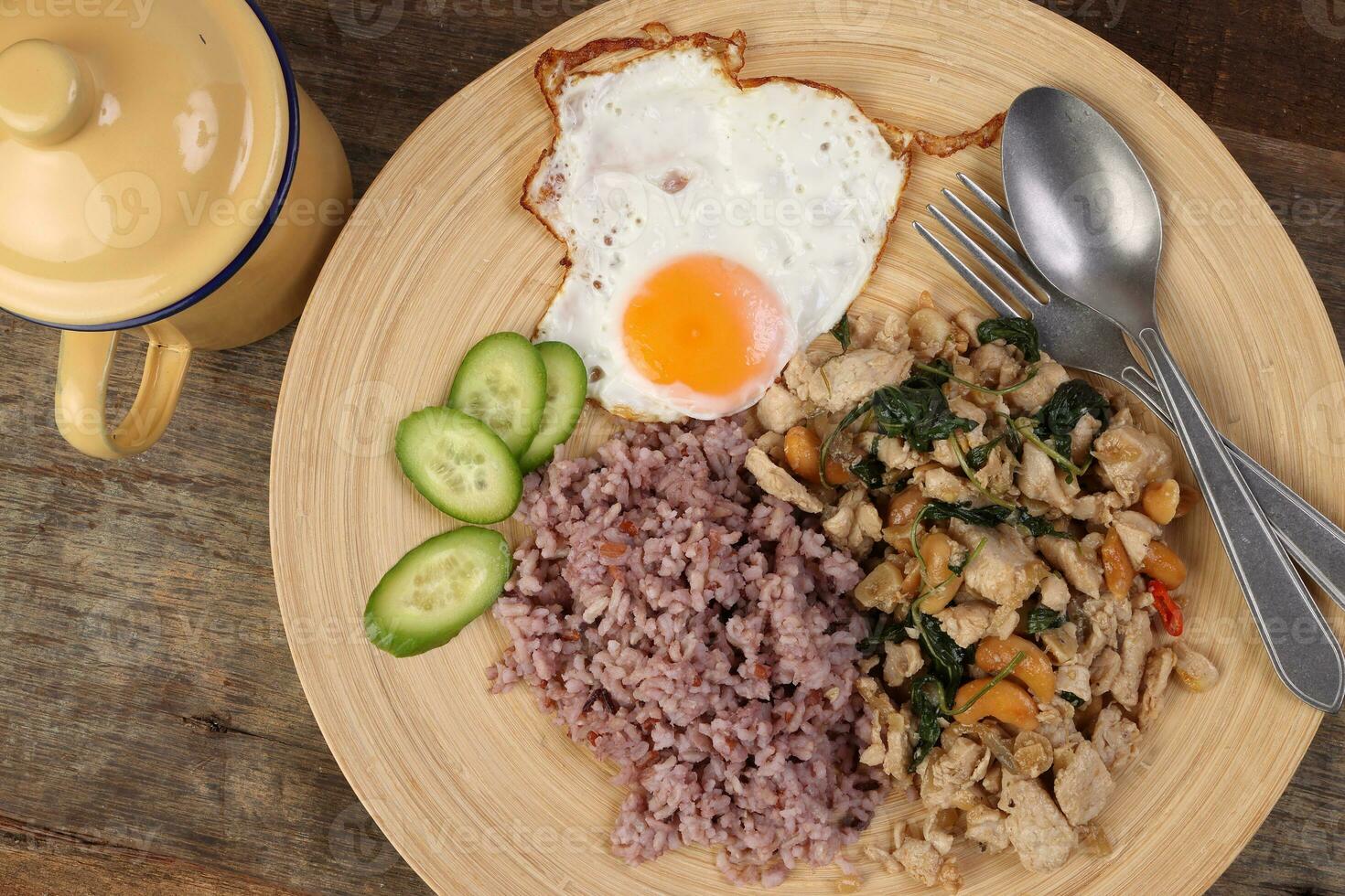 Thai fusion stair fried chicken with Thai basil and cashew nut with health brown rice fried egg sauce cucumber on woody plate over rustic wood background tin mug fork spoon photo