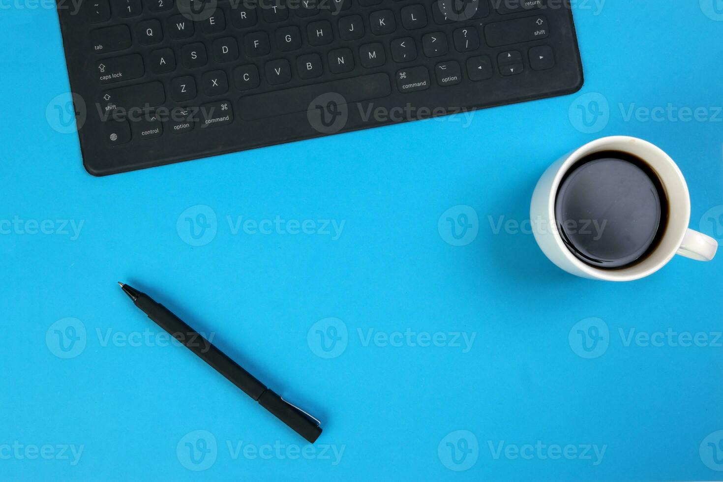 Black computer keyboard coffee cup pen on blue white background top view copy text space photo
