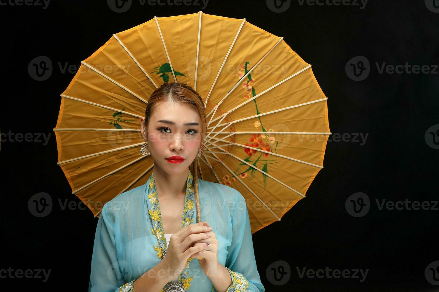 Asian woman in tractional kebaya behind umbrella on black background photo