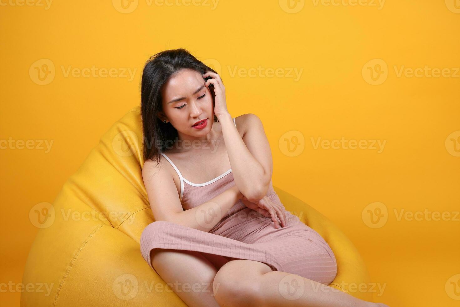 Beautiful young south east Asian woman sit on a yellow orange beanbag seat color background relax rest think emotion imagine expression pose photo