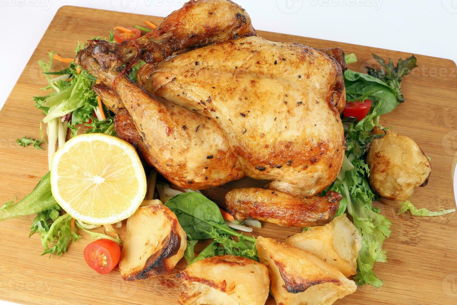 Whole roasted grilled chicken poultry bird with baked potato vegetable salad tomato lemon on wooden cutting board white background photo