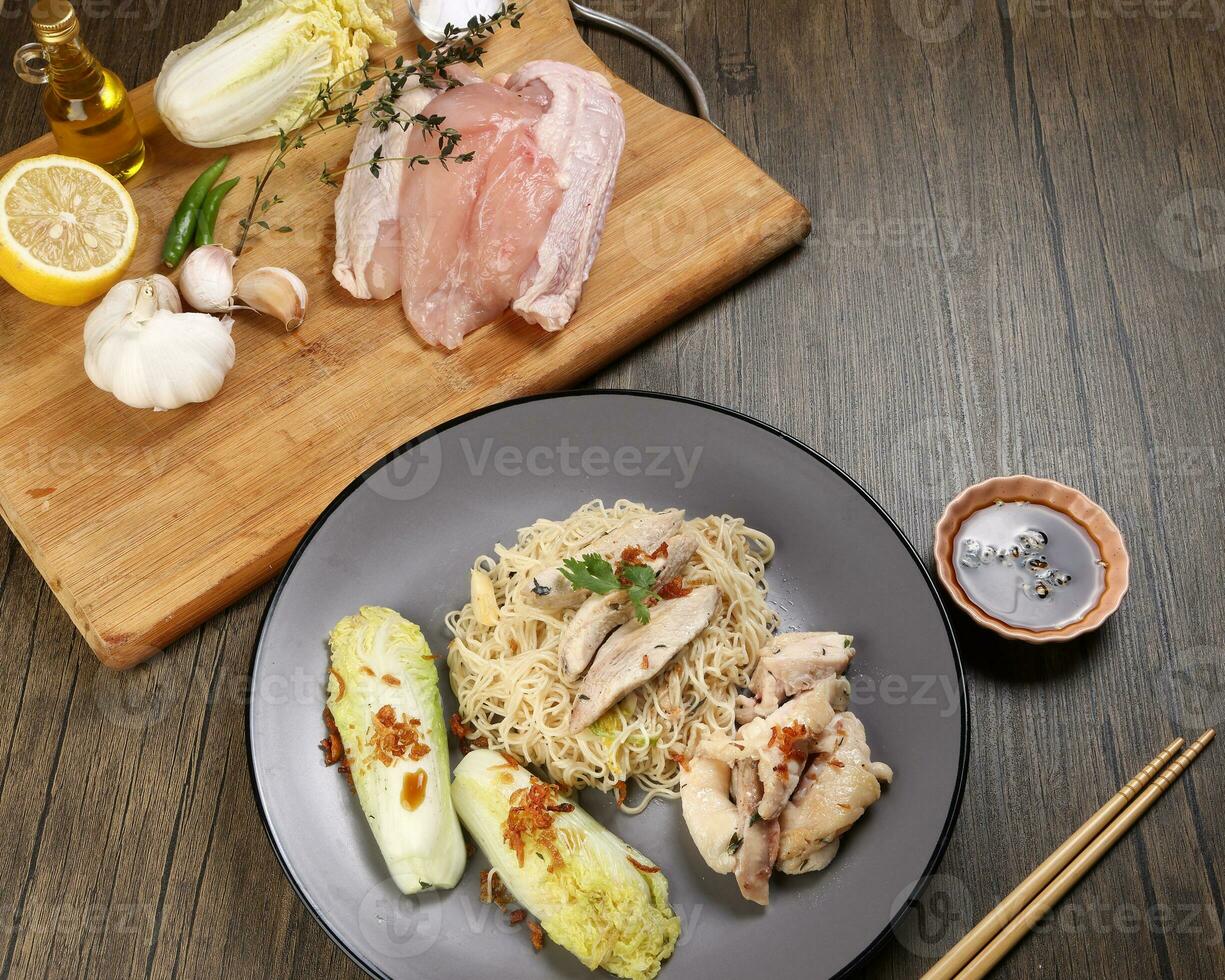 Asian western fusion fried noodles sliced chicken breast thyme garlic ginger chilli Chinese cabbage onion lemon served on grey plate chopsticks soya sauce on wooden table raw ingredients photo