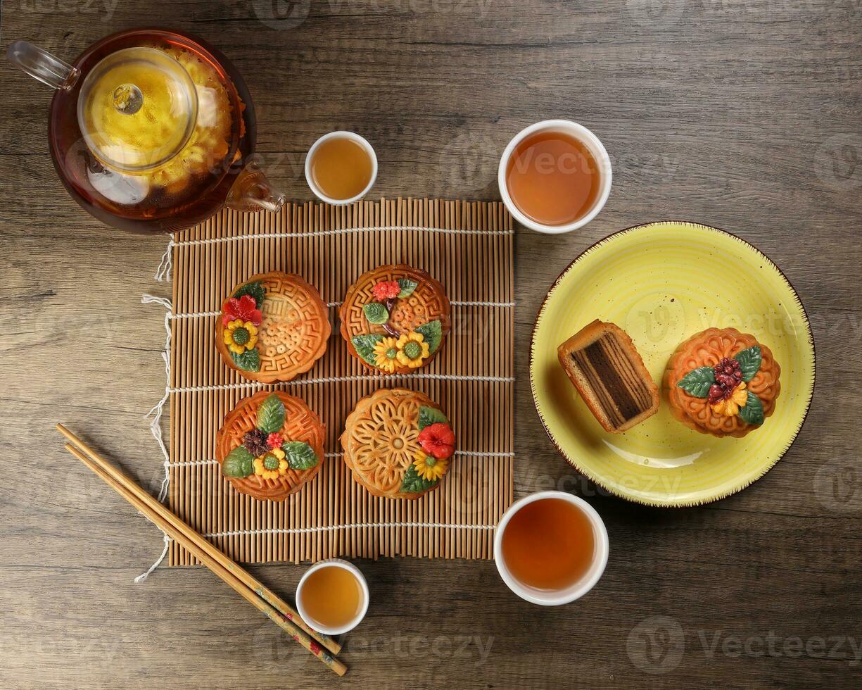 Colourful flower decorated mooncake Chinese mid autumn festival on bamboo food mat background slice cut piece layered on yellow ceramic plate glass teapot teacup chopsticks photo