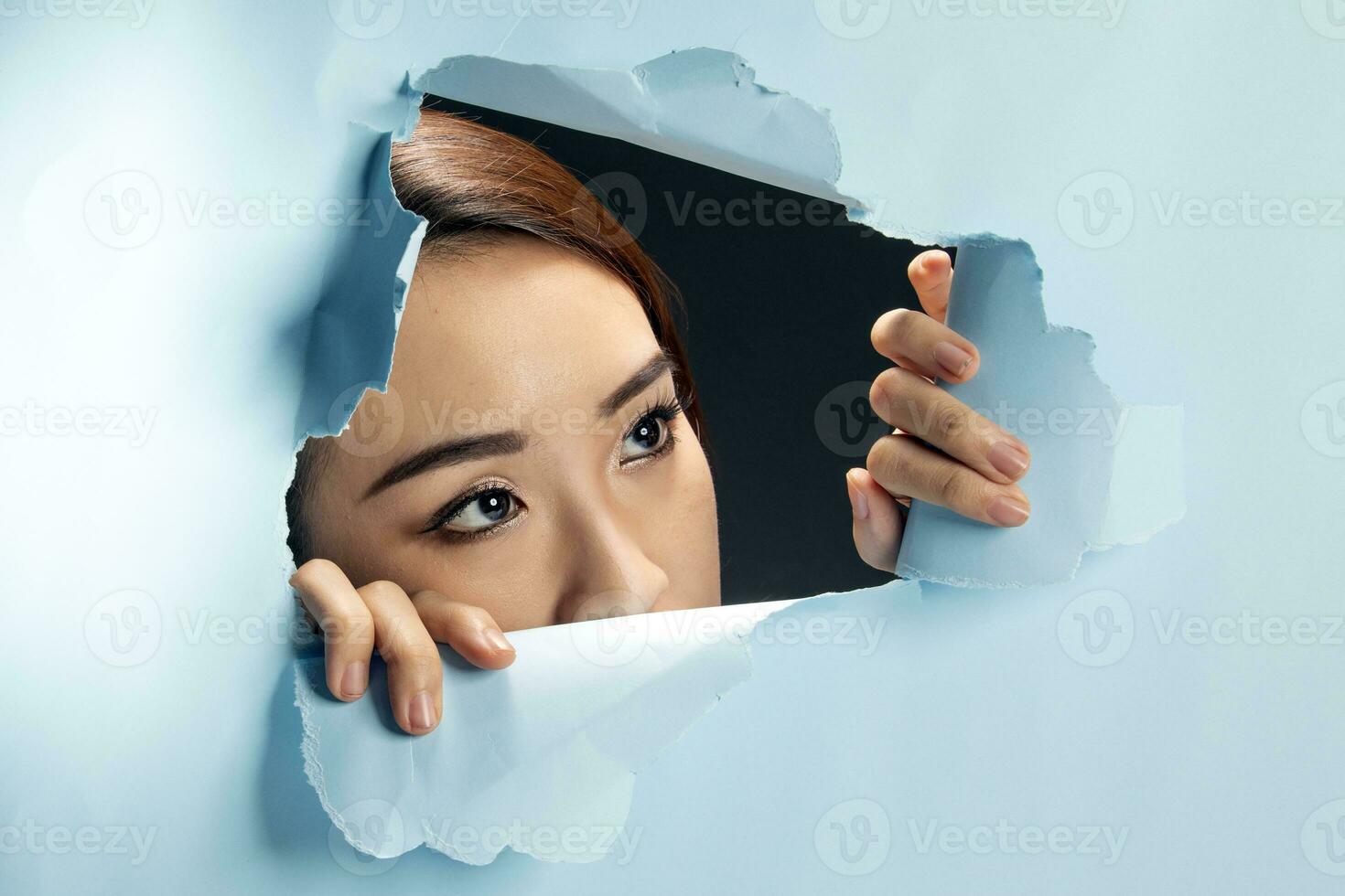 Young beautiful Asian woman expression through torn paper hole photo