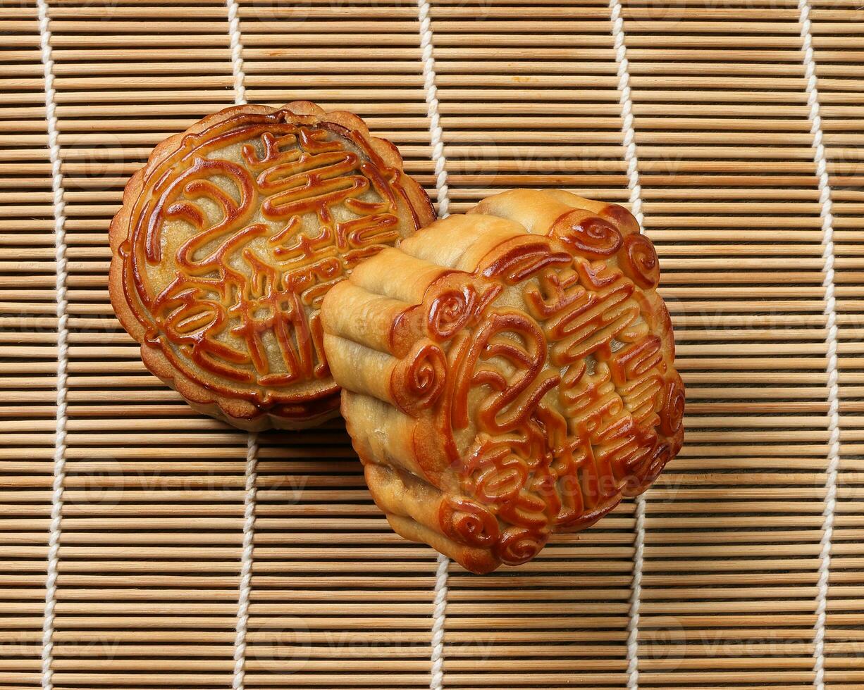 Chinese baked decorated mooncake mid autumn festival square round moon cake filling gift wish offering on bamboo mat over wooden table mini cup photo