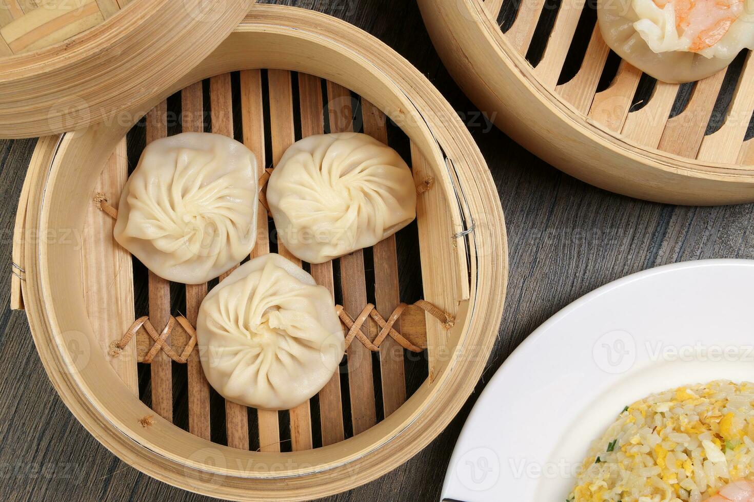 Prawn shrimp shaomai Xiao long bao dim sum dumpling chicken prawn fish seafood vegetable in bamboo steamer fried rice on plate sauce chopsticks soup spoon over rustic background photo