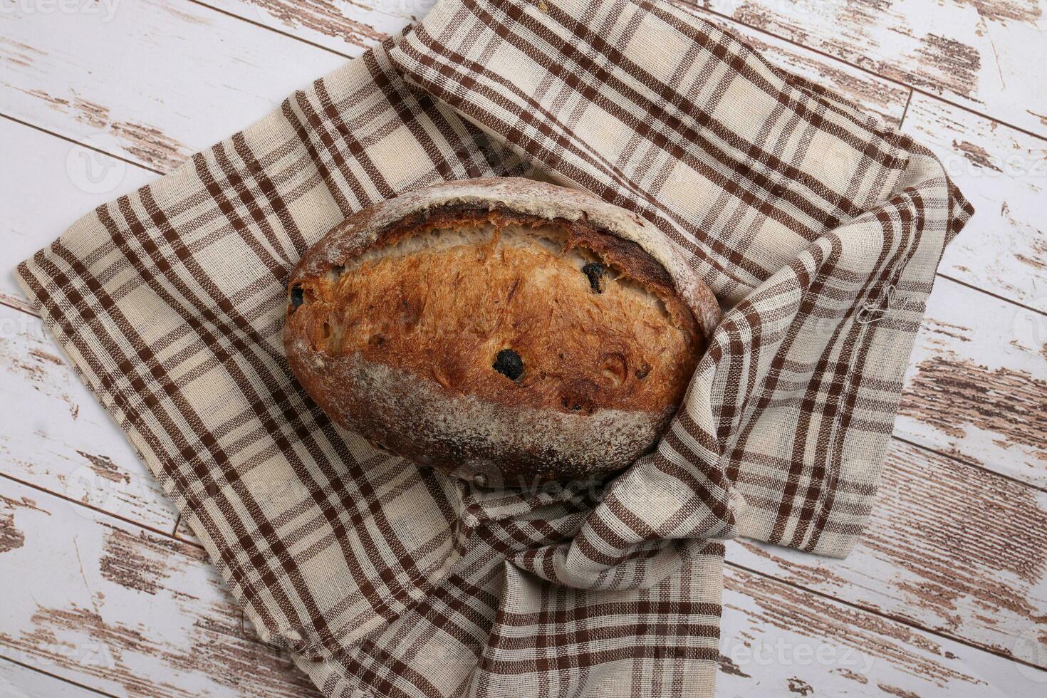 Rustic whole grain artisan bread loaf with cranberry raisin dry fruit nuts wrapped in checkers cloth with wooden table top flat lay view photo