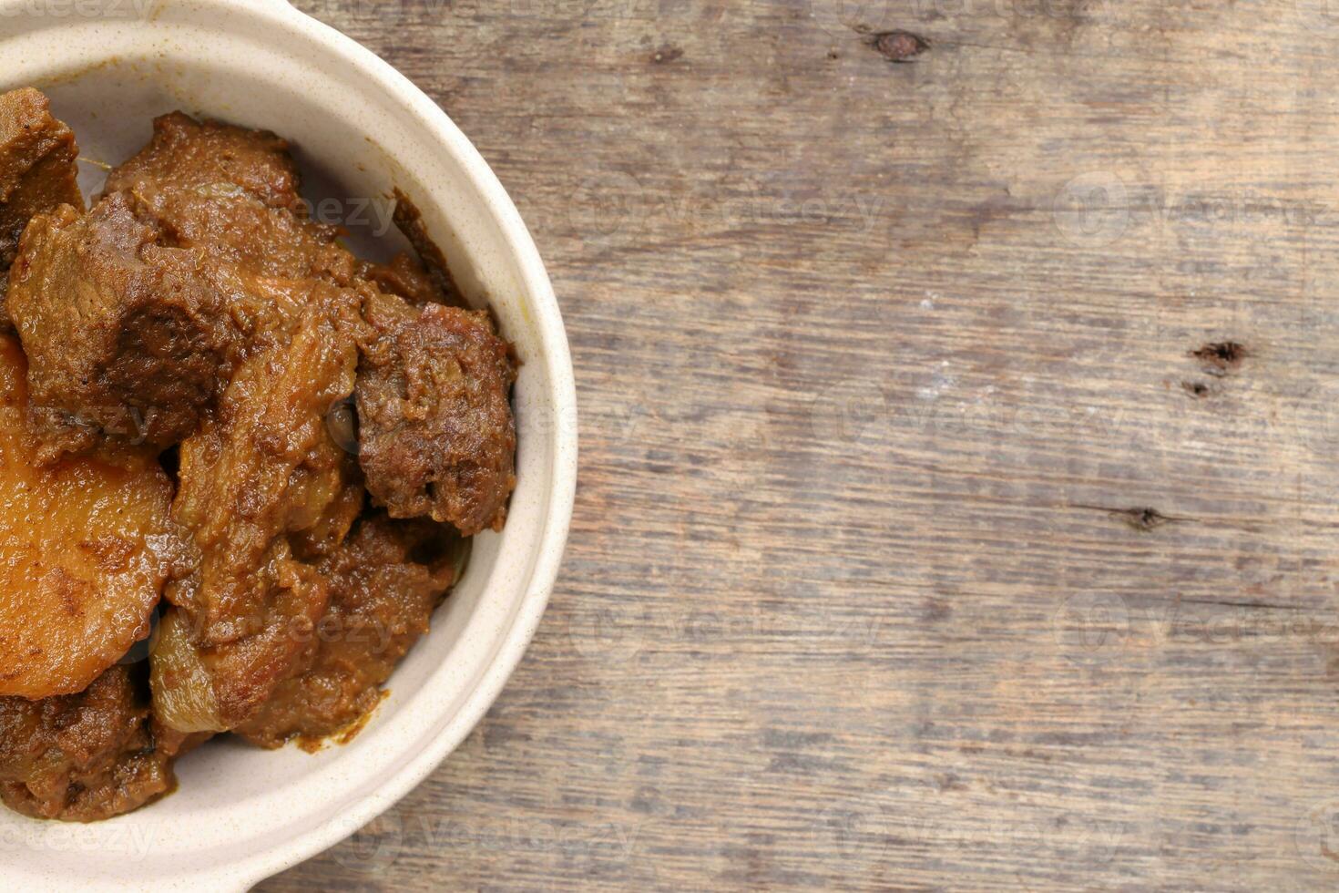 Asian style Beef bhuna dry curry with potato in ceramic bowl over rustic wooden background photo