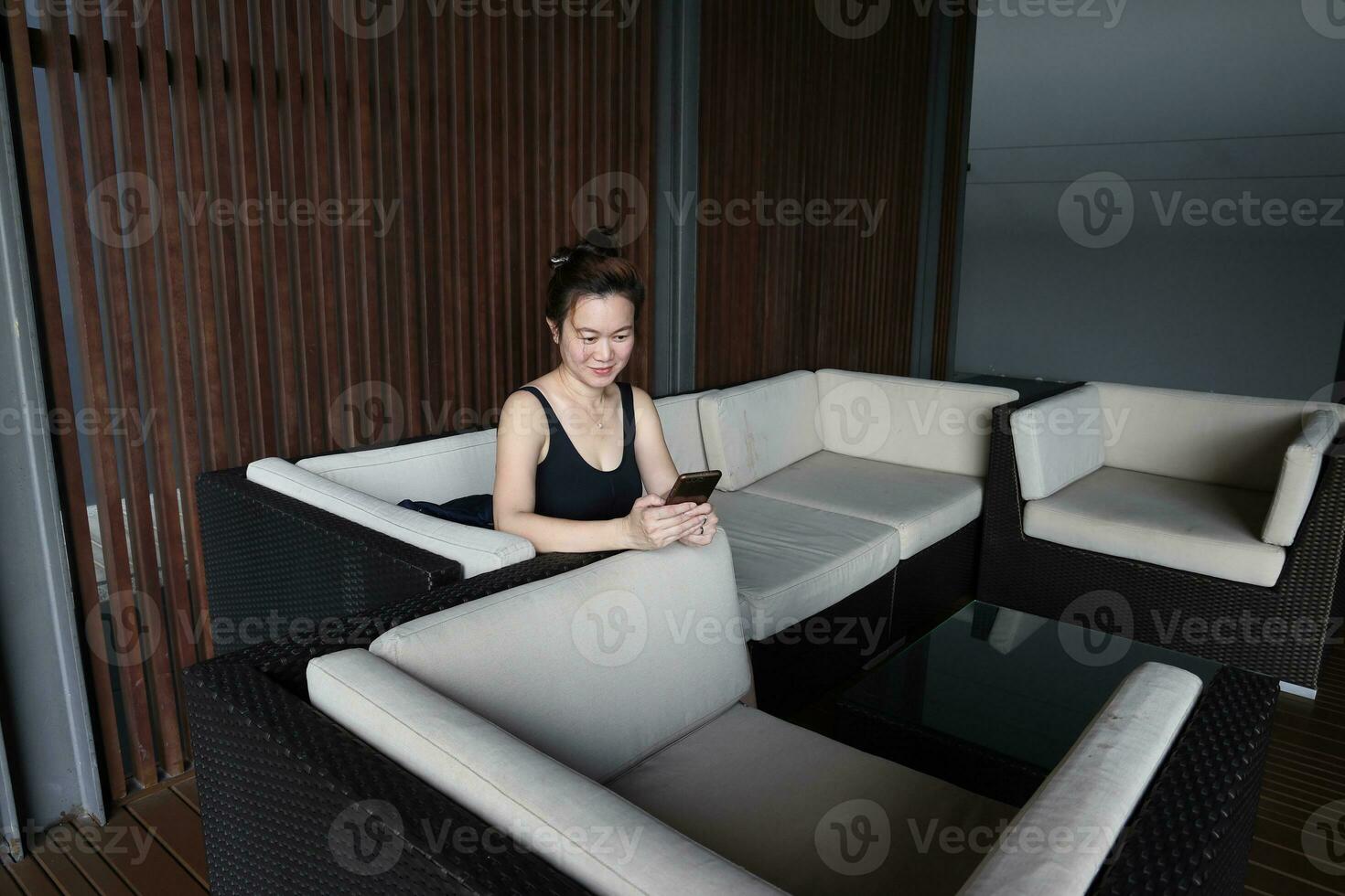 beautiful attractive middle age southeast asian woman resting sitting on sofa after exercise text looking smart phone dark wooden background waiting resting area photo