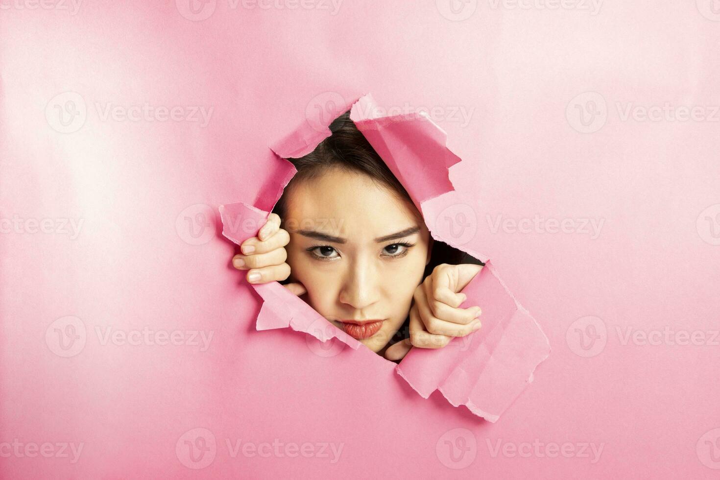 Young beautiful Asian woman expression through torn paper hole photo