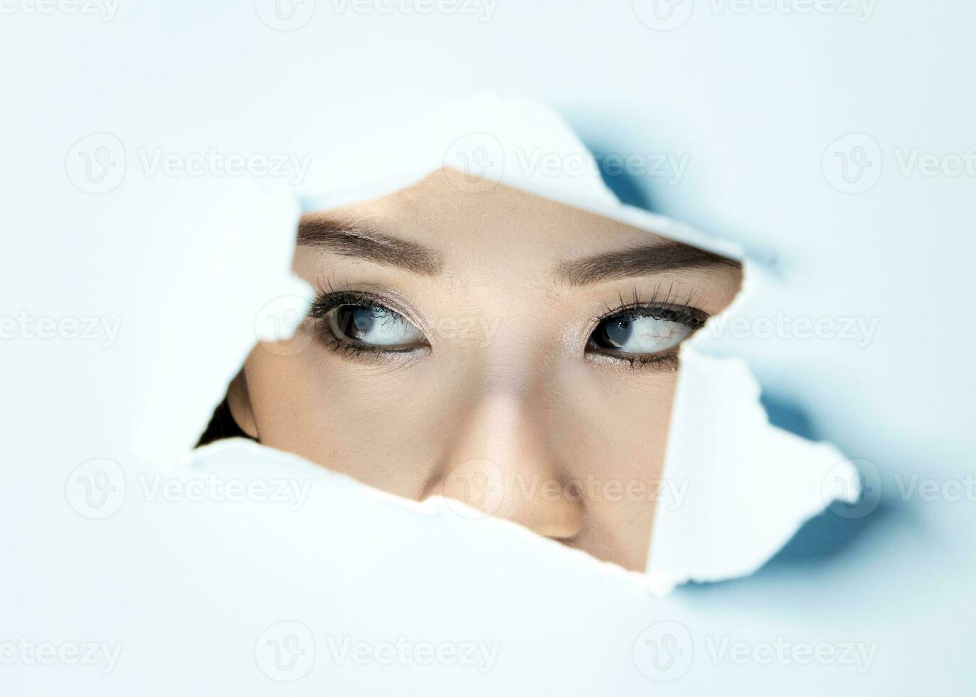 Young beautiful Asian woman expression through torn paper hole photo