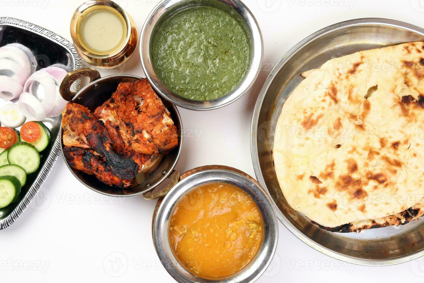 Spicy red Chicken grilled tikka tandoori nan bread green spinach curry yogurt sauce dal tomato cucumber onion salad set in metal stainless steel brass copper pot on white background photo