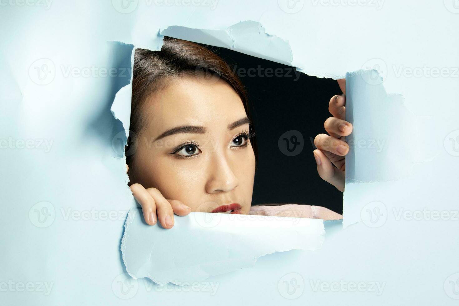 Young beautiful Asian woman expression through torn paper hole photo