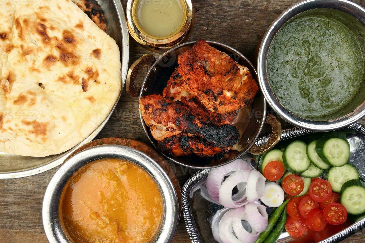 Spicy red Chicken grilled tikka tandoori nan bread green spinach curry yogurt sauce dal tomato cucumber onion salad set in metal stainless steel brass copper pot on rustic vintage wood background photo