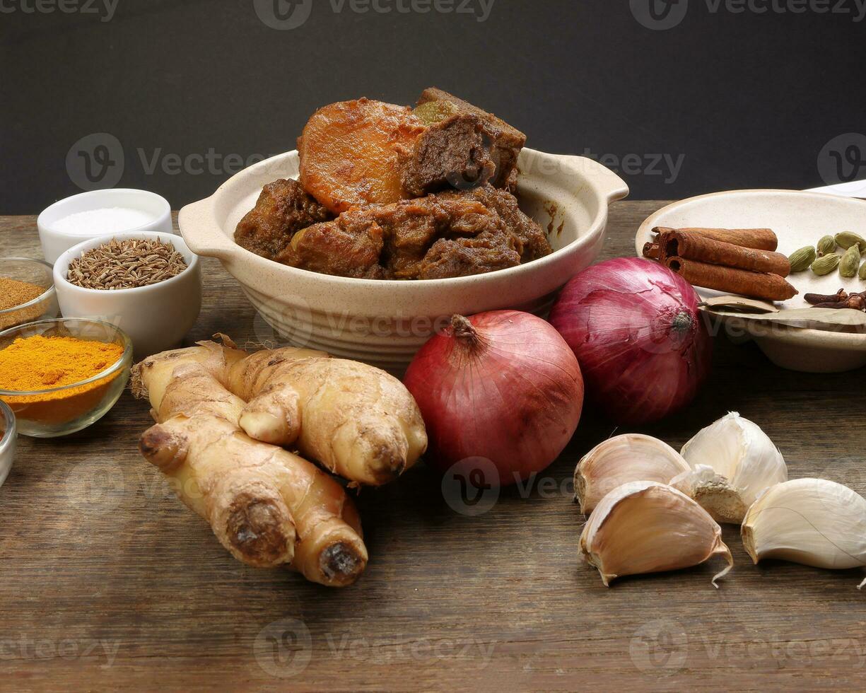 Beef bhuna dry curry with potato in ceramic bowl ingredients chilli cumin coriander turmeric powered salt onion garlic ginger bay leaf cinnamon cardamom clove over rustic wood background photo