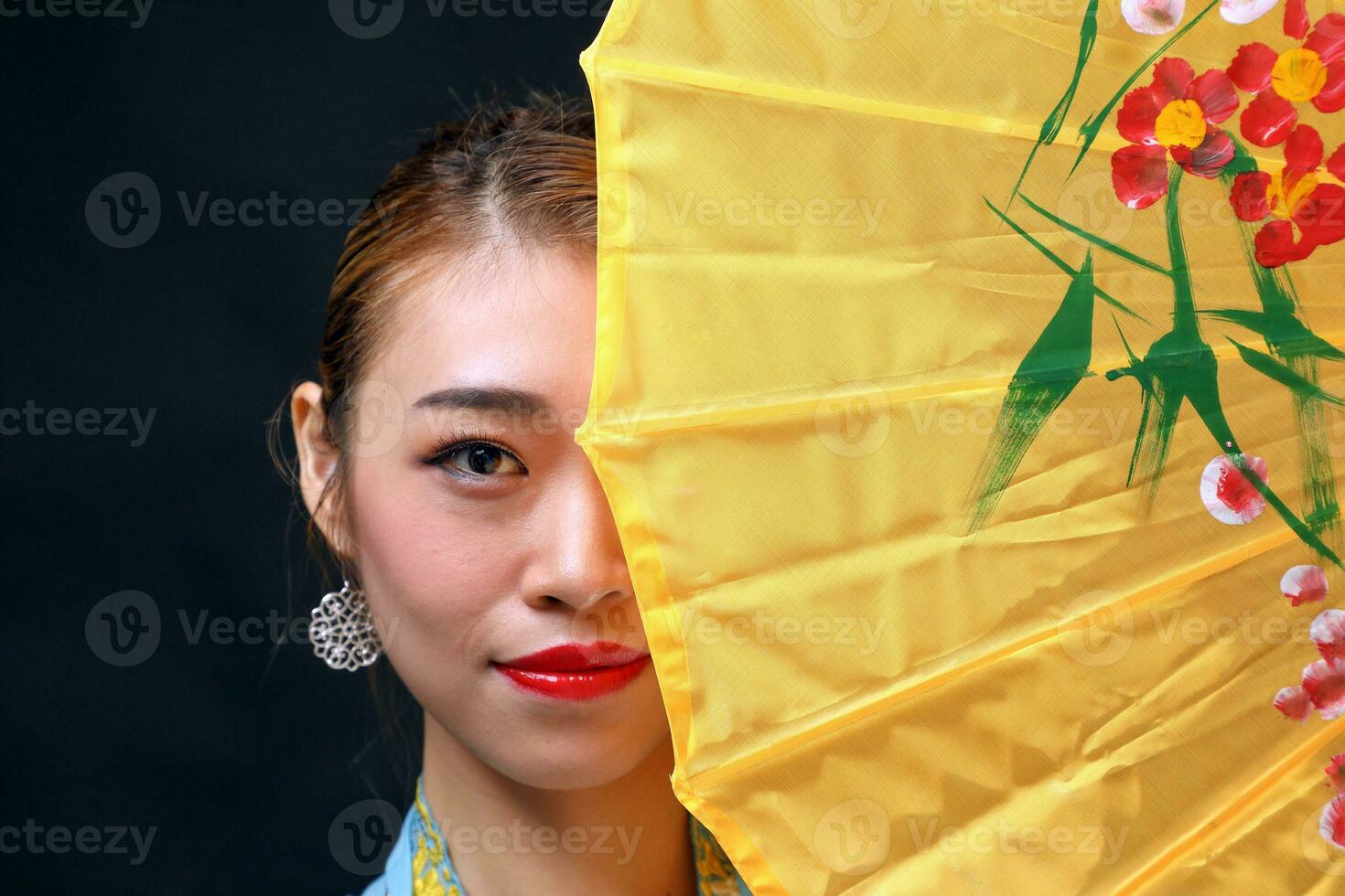 Asian woman in tractional kebaya behind umbrella on black background photo