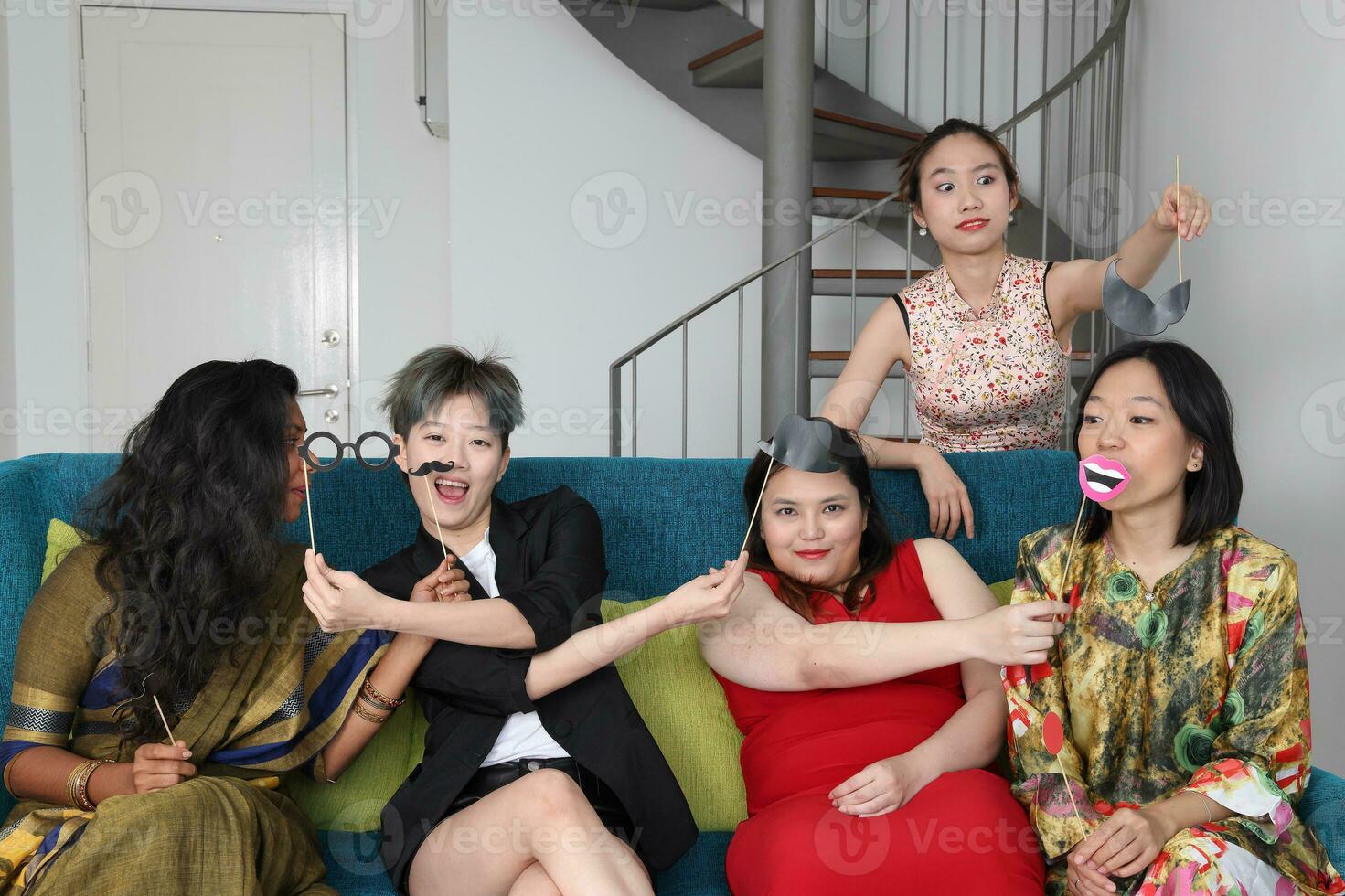 Young Asian woman group talk sing making funny mocking faces expression selfie portrait paper props mustache hat pipe nose hair on blue living room sofa sit photo