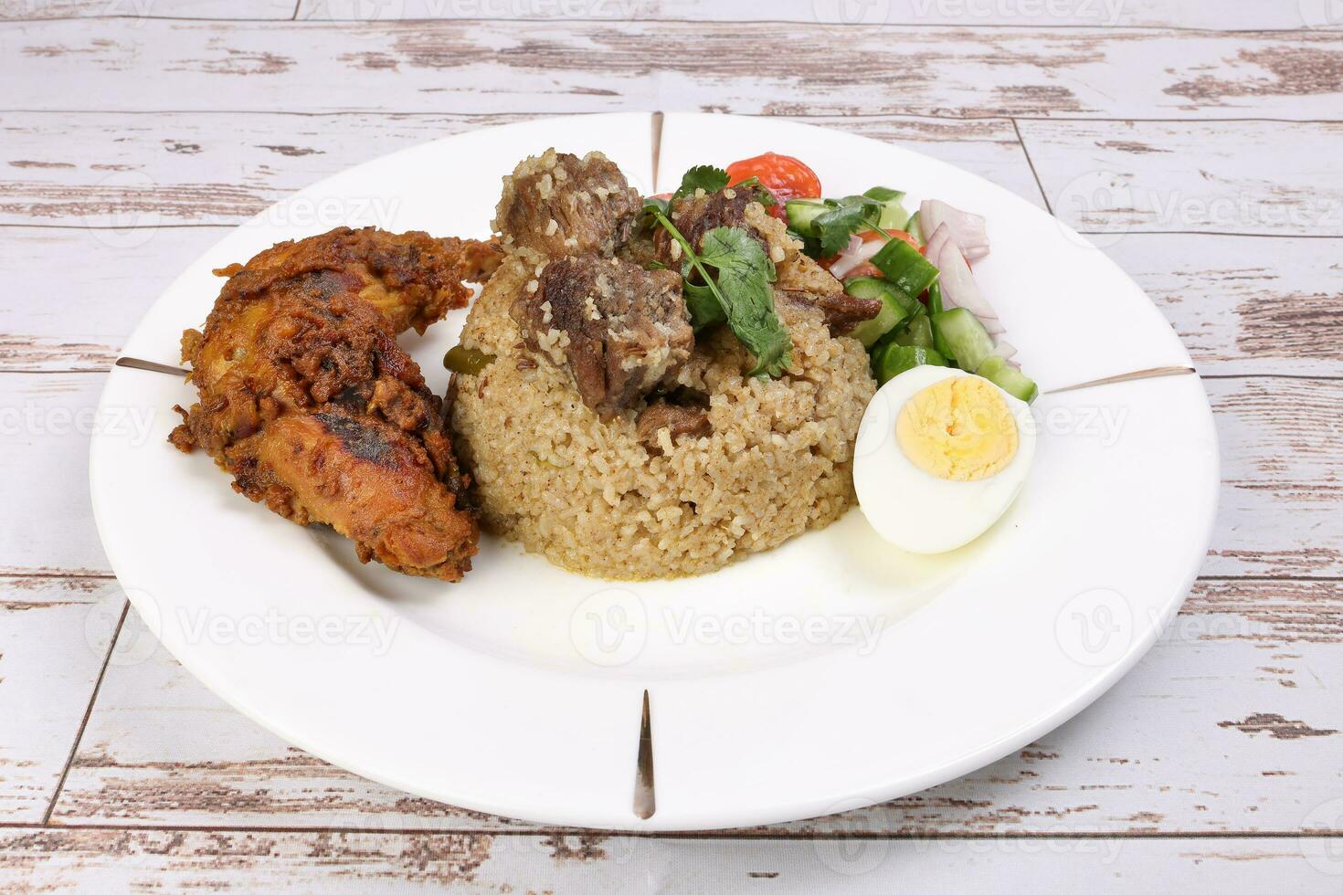 Beef Biryani Tehari with boiled egg coriander leaf garnish chicken curry pot roasted leg tomato cucumber onion chili coriander salad on white plate set over rustic wood background photo