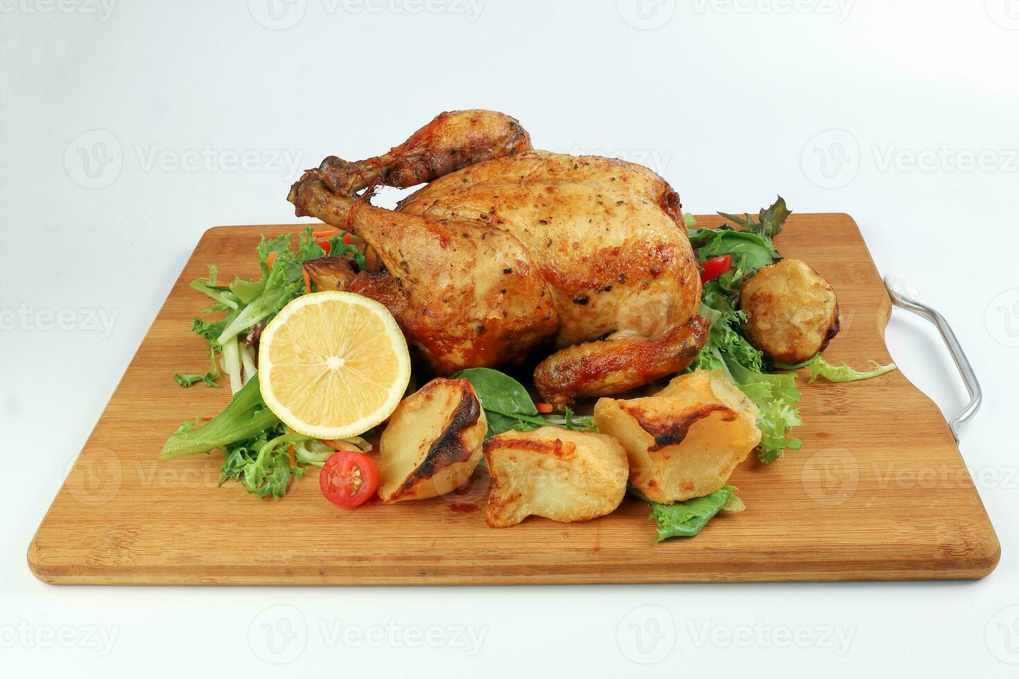 Whole roasted grilled chicken poultry bird with baked potato vegetable salad tomato lemon on wooden cutting board white background photo