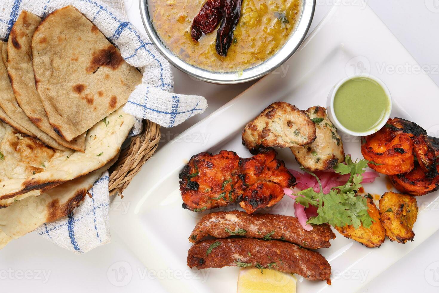 Mixed grill kebab chicken mutton beef prawn fish mint sauce lemon pickled onion bread basket chapati naan tandoori paratha dal lentil fry tadka copper pot on white dish over white background photo