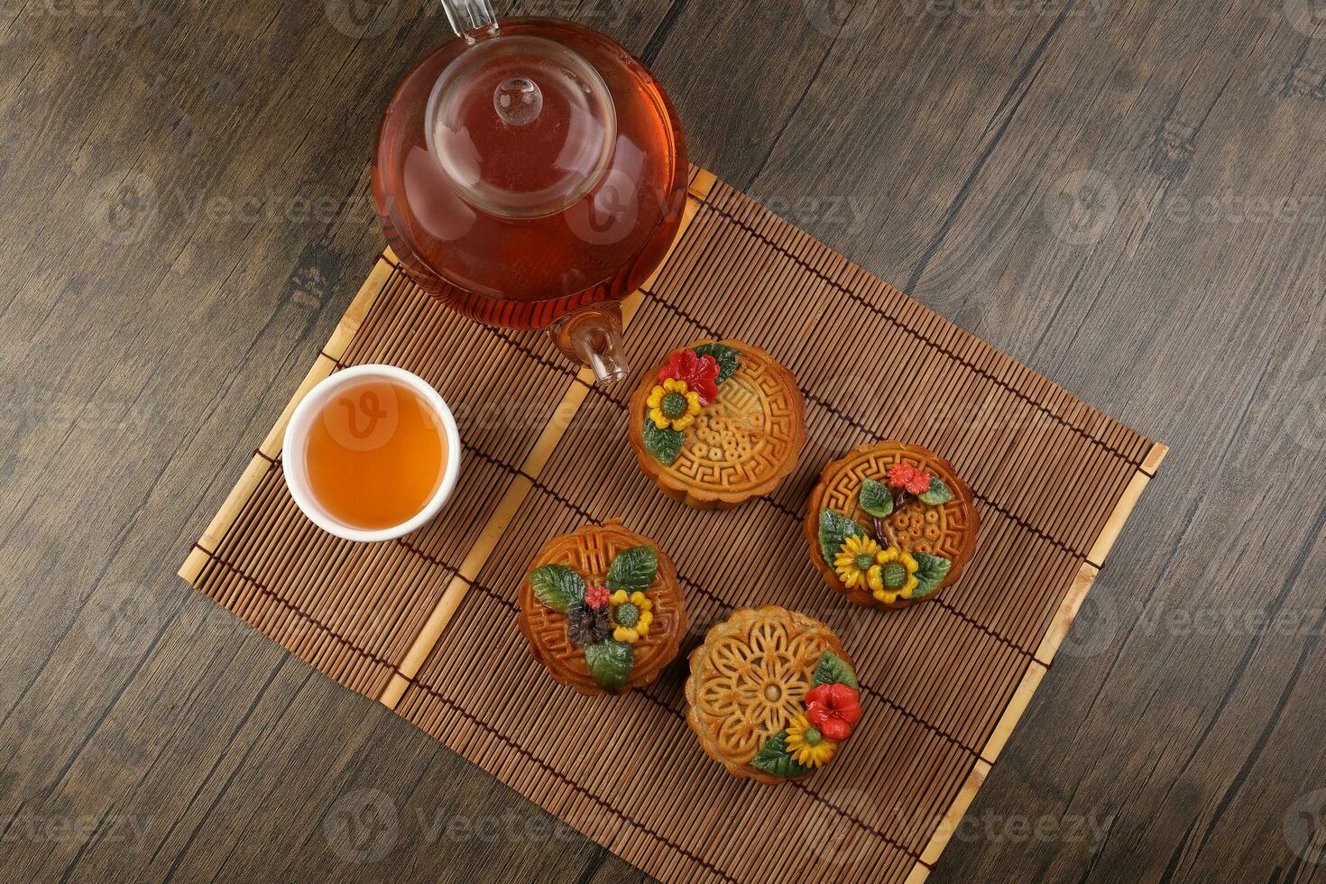 Colorful flower decorated mooncake cut slice half layer Chinese mid autumn festival on bamboo food mat glass teapot white ceramic teacup photo