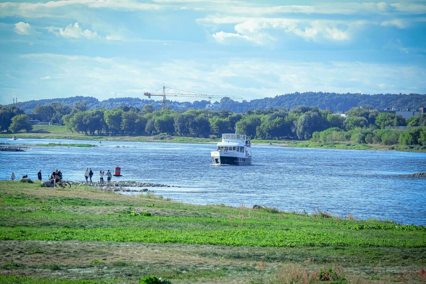 Kaunas, Lithuania 20 10 2022 Small white vessel coming to the shore on river blue water while people are waiting on the bank on sunny day photo