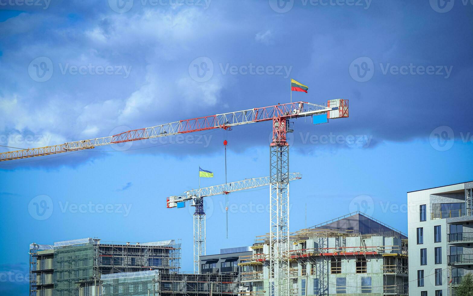 Construction site with cranes with flags Lithuanian and Ukrainian building residential buildings on blue sky background with fluffy dark clouds photo