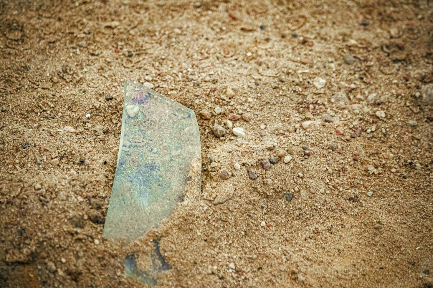 Transparent sharp glass shard from sticking out of the sand on the rural road with small pebbles photo