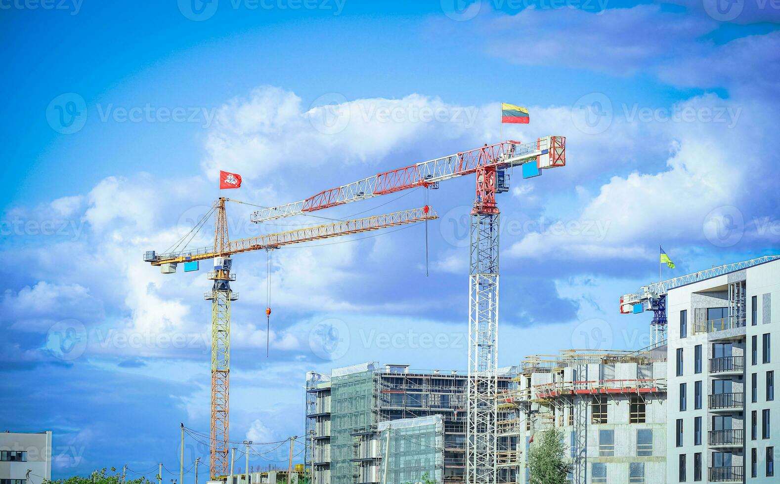 Construction site with cranes with flags Lithuanian and Lithuanian coat of arms building residential buildings on blue sky background with fluffy white clouds photo