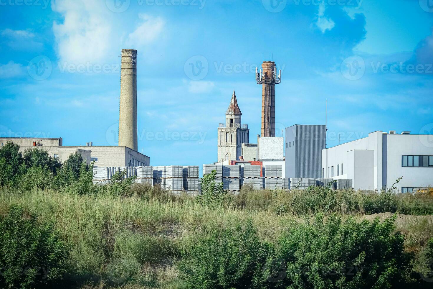 Construction site building blocks with church building huge pipe and visible residential houses surrounded by greenery on sunny day photo