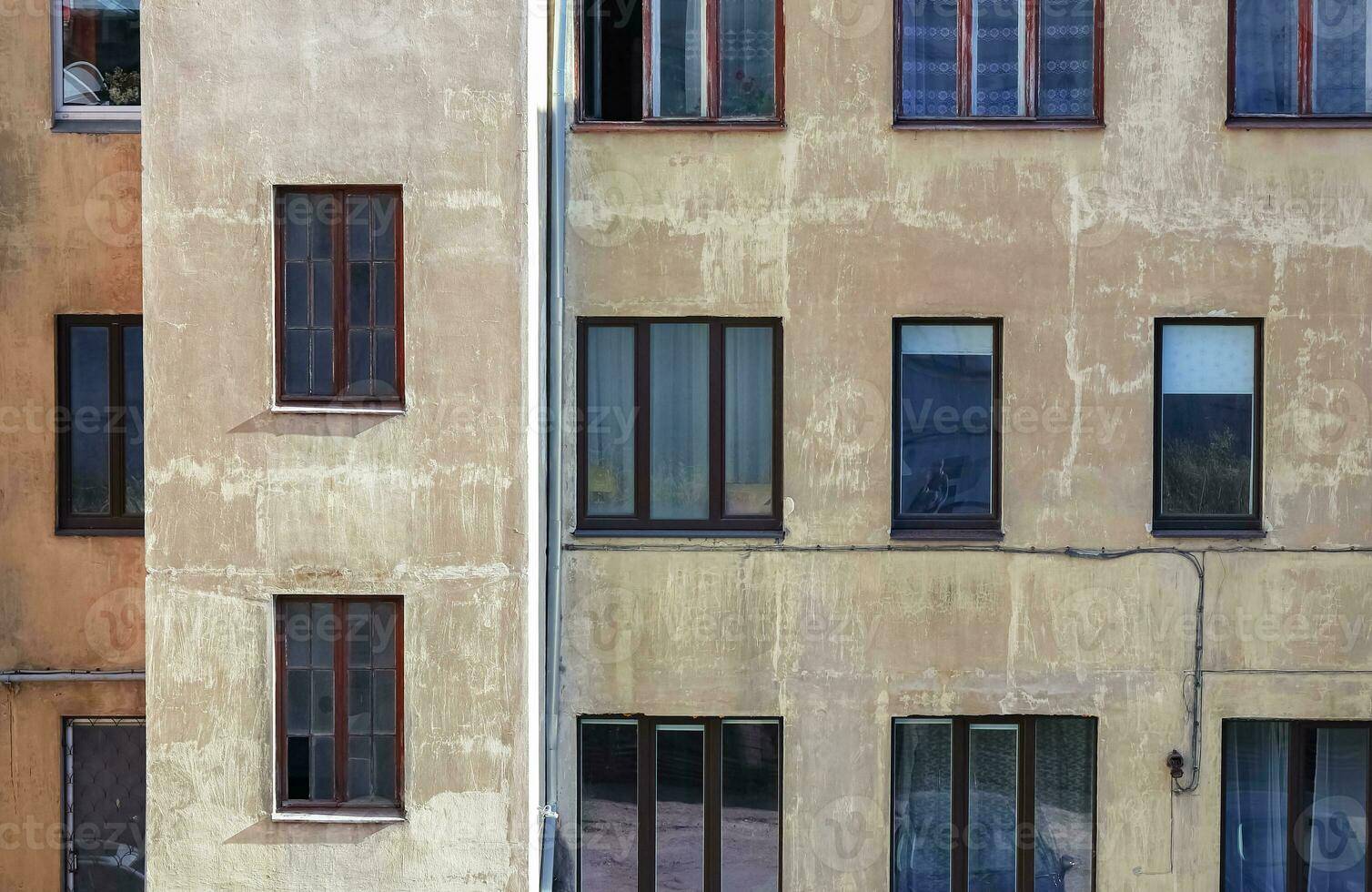 Wall of brown building with stailess steel water pipe and many different windows with various objects and people inside photo