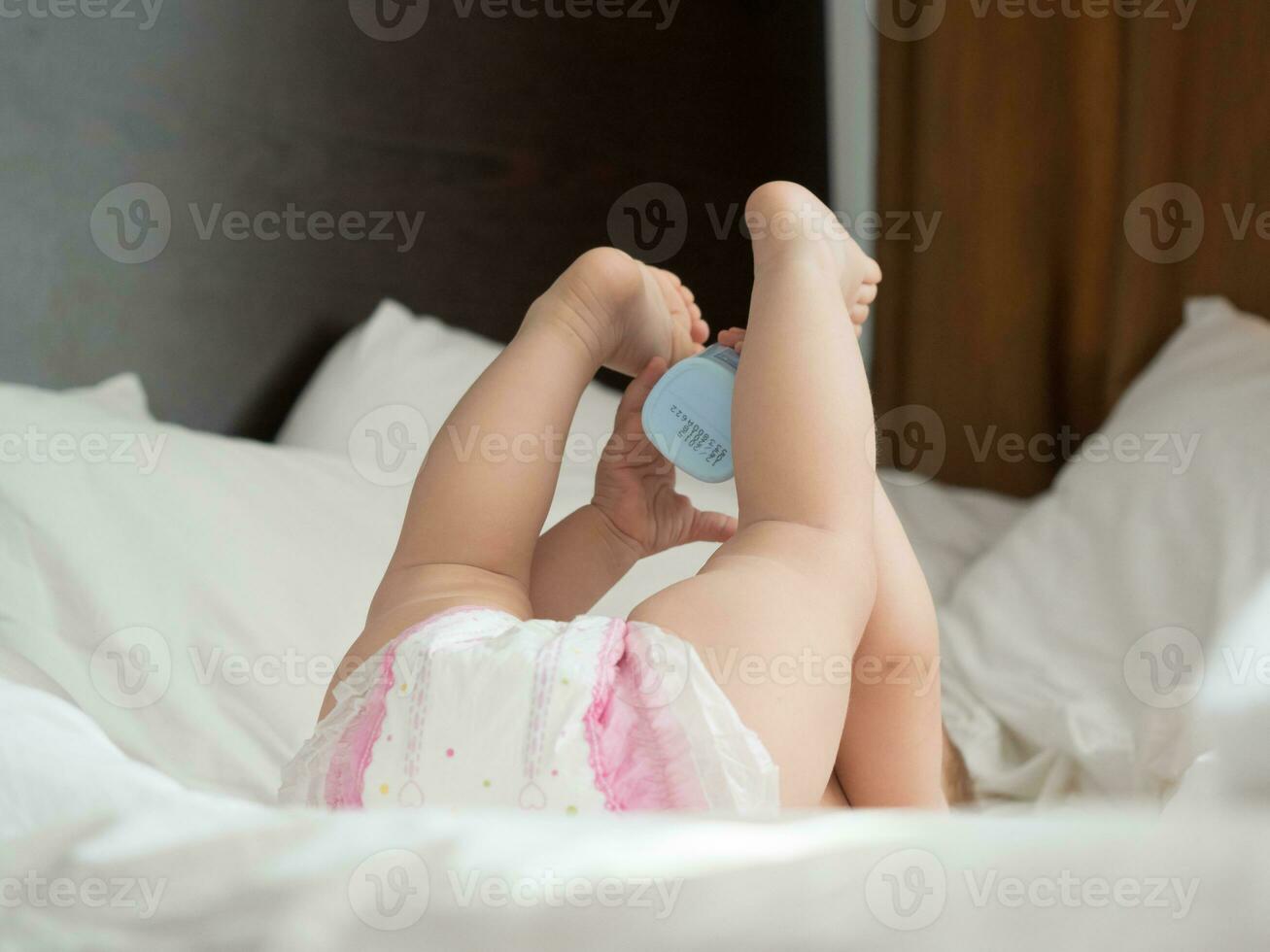 Baby with diaper lying on bed with legs raised up photo