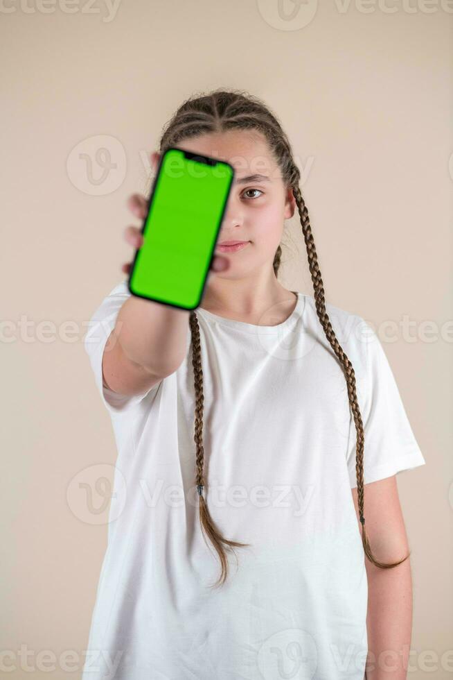 Young girl showing smartphone with green screen isolated on beige background photo