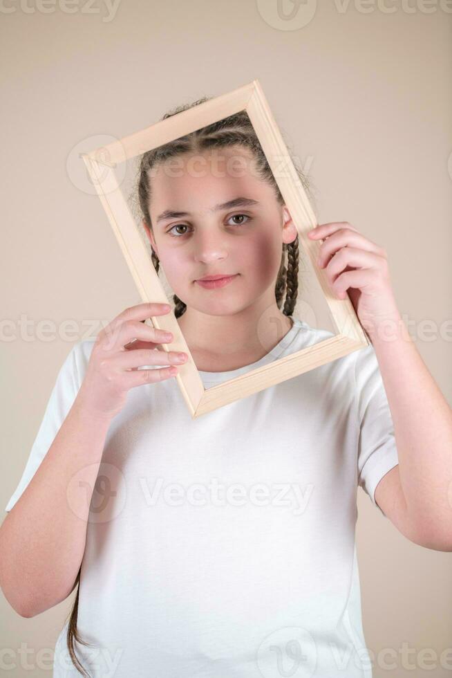 retrato de un linda pequeño niña participación un imagen marco. estudio Disparo foto