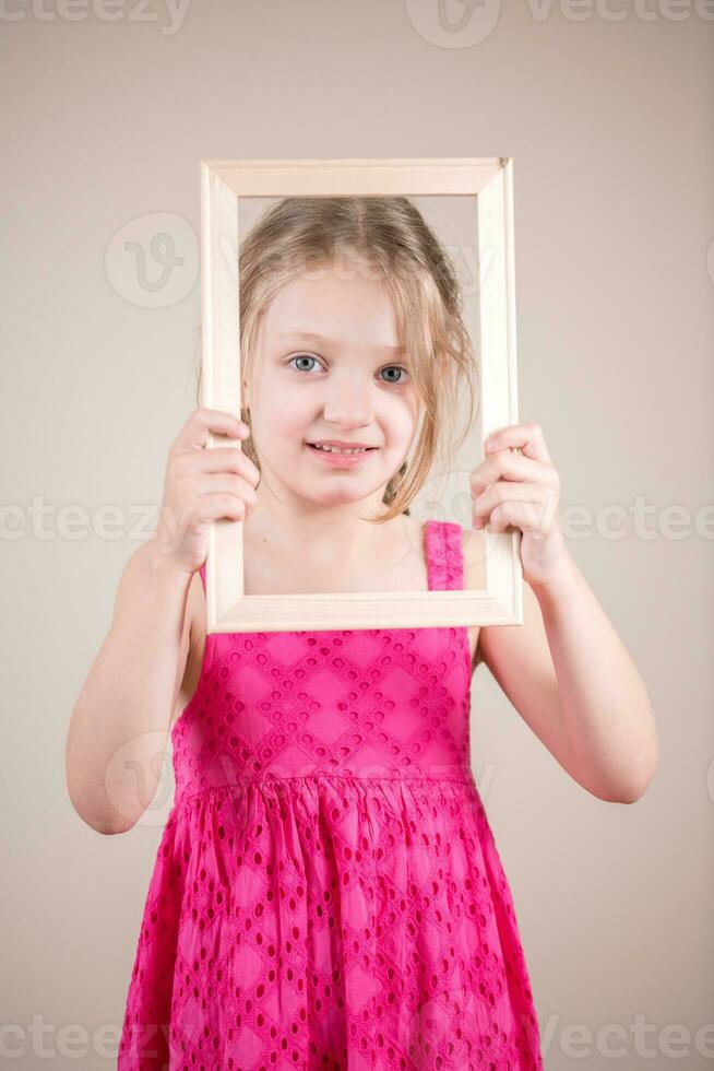 retrato de un linda pequeño niña participación un imagen marco. estudio Disparo foto