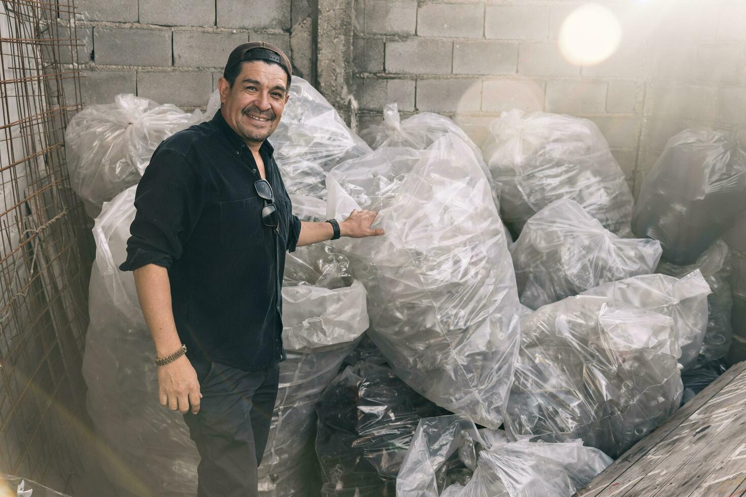 hombre sonriente y mirando a cámara demostración su reciclaje trabajar, pantalones lleno de el plastico botellas foto