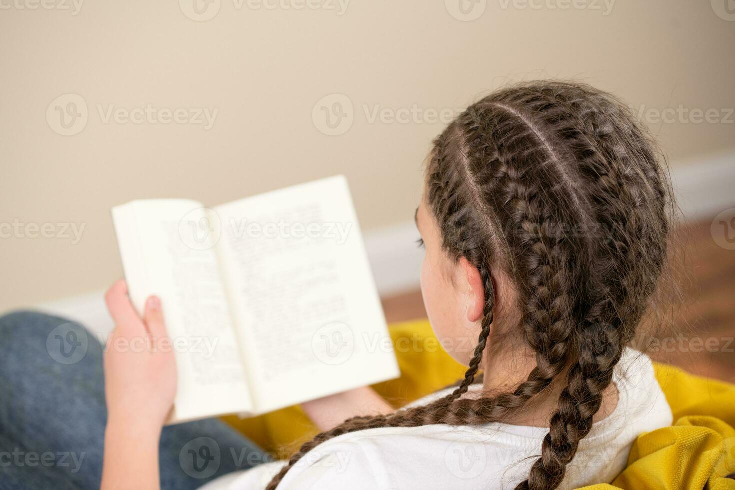 Adolescente niña con trenzas leyendo libro en amarillo bolsa de frijoles silla foto