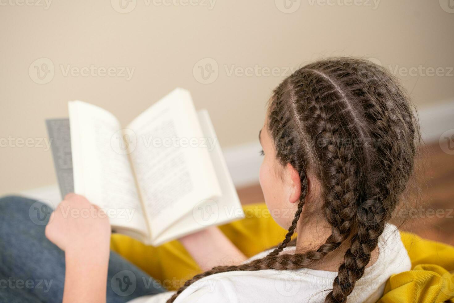 Teenage girl with braids reading book on yellow beanbag chair photo