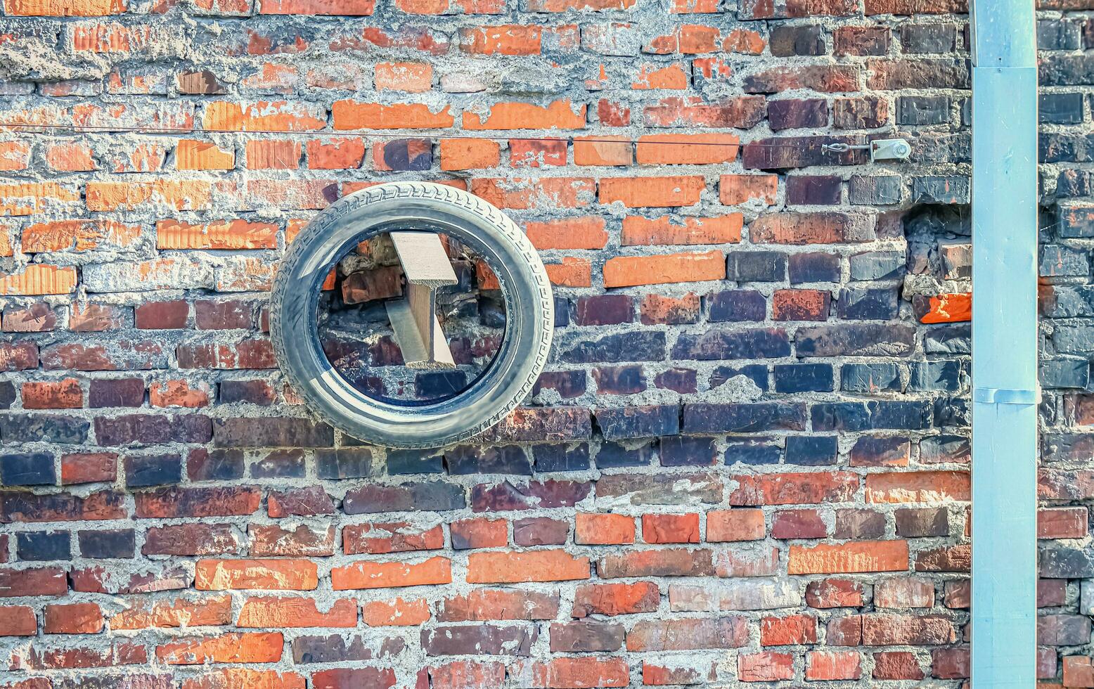 Black rubber tire hanging on wooden detail of red brick wall building with stailess steel water pipe on a side on sunny day photo