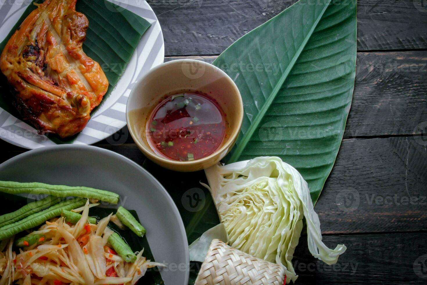Thai food dish both in Thailand and Asia Papaya Salad or as we call it Somtum is complemented with grilled chicken and sticky rice with fresh stir-fries. Served on the black wooden table. photo