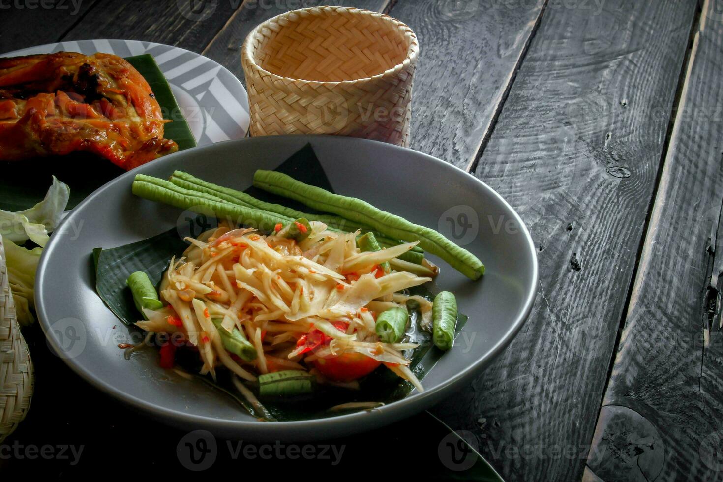 tailandés comida plato ambos en Tailandia y Asia, papaya ensalada o como nosotros llamada eso somtum es complementado con A la parrilla pollo y pegajoso arroz con Fresco frituras. servido en el negro de madera mesa. foto