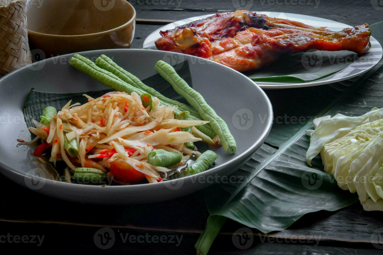 Thai food dish both in Thailand and Asia, Papaya Salad or as we call it Somtum is complemented with grilled chicken and sticky rice with fresh stir-fries. Served on the black wooden table. photo