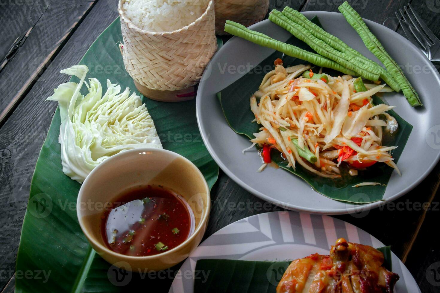 Thai food dish both in Thailand and Asia Papaya Salad or as we call it Somtum is complemented with grilled chicken and sticky rice with fresh stir-fries. Served on the black wooden table. photo