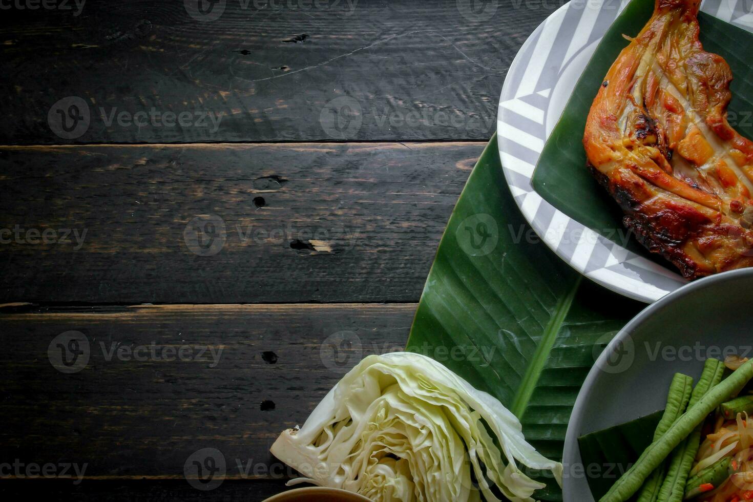 Thai food dish both in Thailand and Asia, Papaya Salad or as we call it Somtum is complemented with grilled chicken and sticky rice with fresh stir-fries. Served on the black wooden table. photo